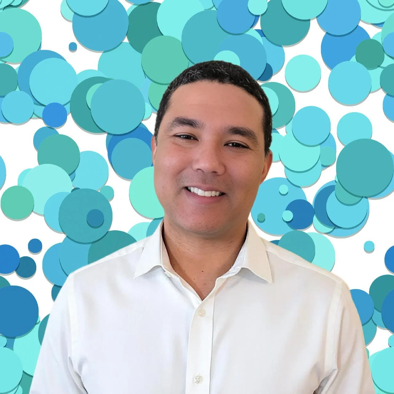 A smiling man with short dark hair wearing a white shirt, standing in front of a background filled with various shades of blue and green circles.