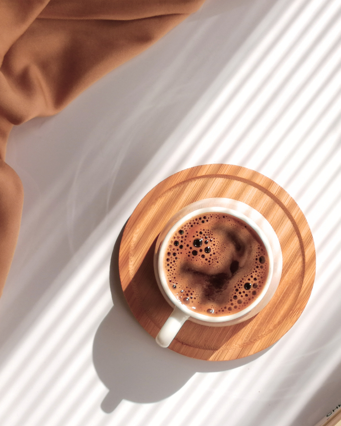En kopp kaffe på ett runt trädbricka med skuggor och ljusreflektioner i bakgrunden.