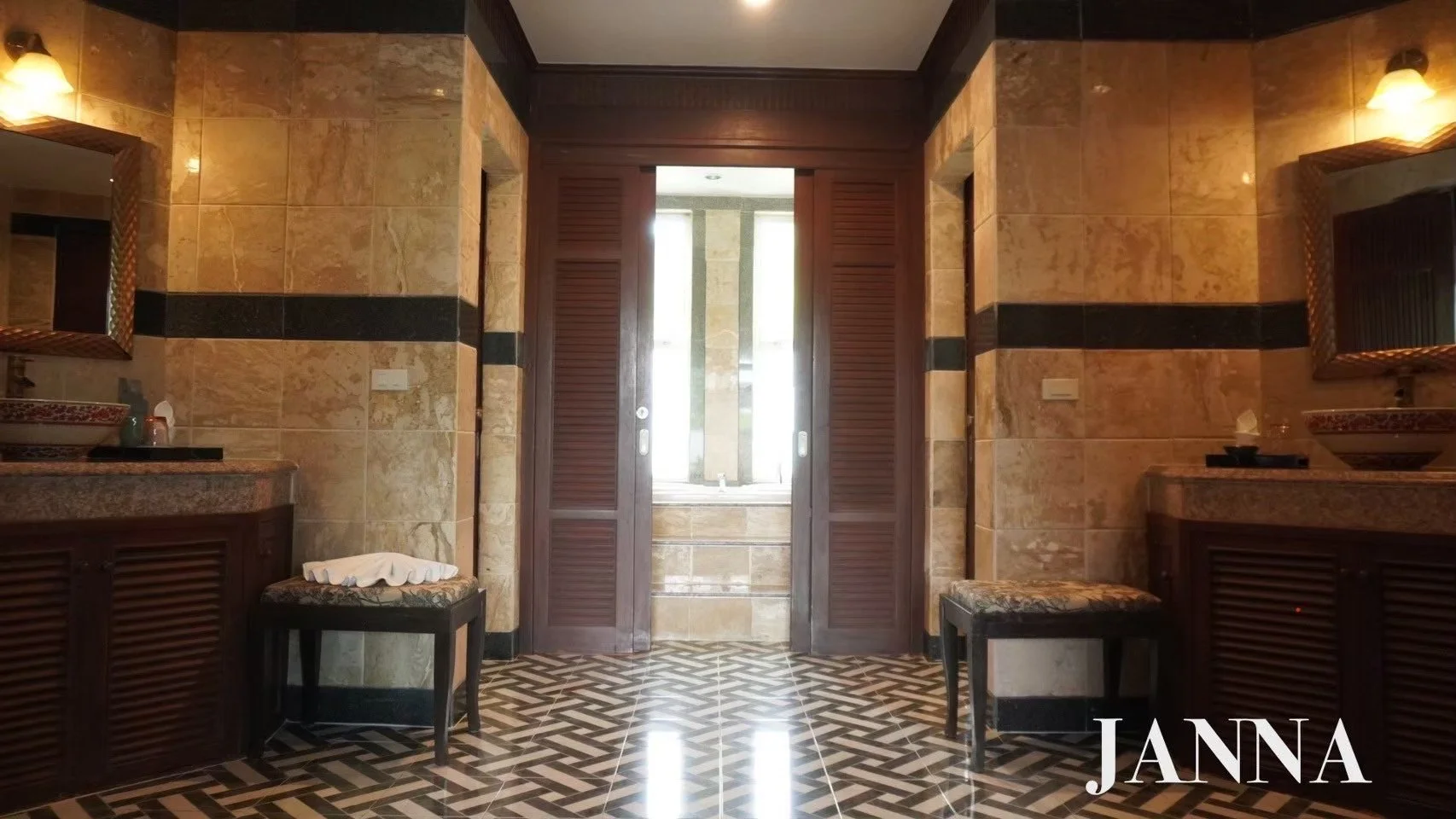 Luxurious bathroom with tiled walls, two sinks with mirrors, and wooden shutters on window, reflecting a high-end design.