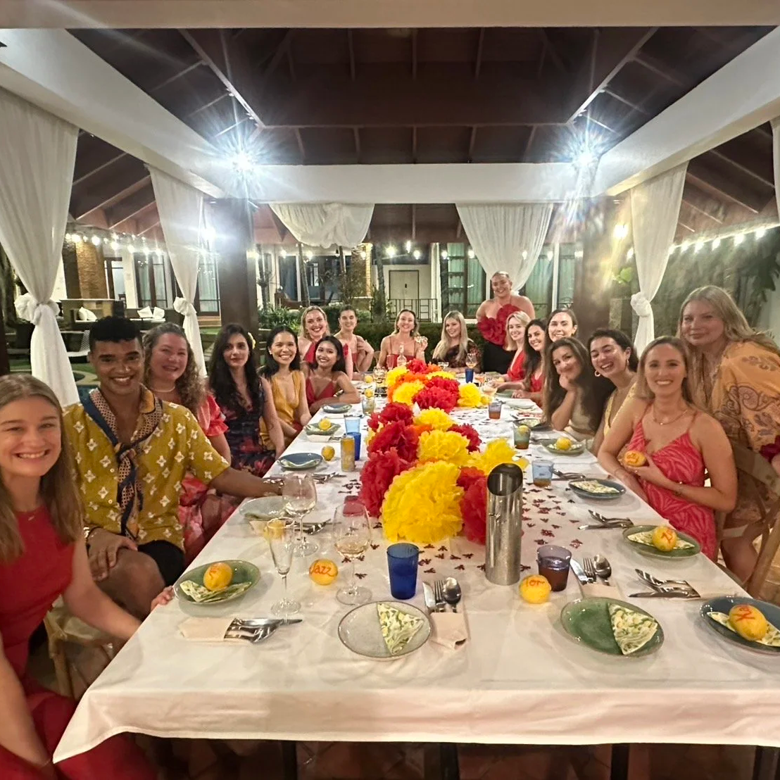 Group of women celebrating at a long decorated dinner table with floral centerpiece, dinnerware, and colorful table decorations in a well-lit indoor venue. corporate retreat large group best villa phuket