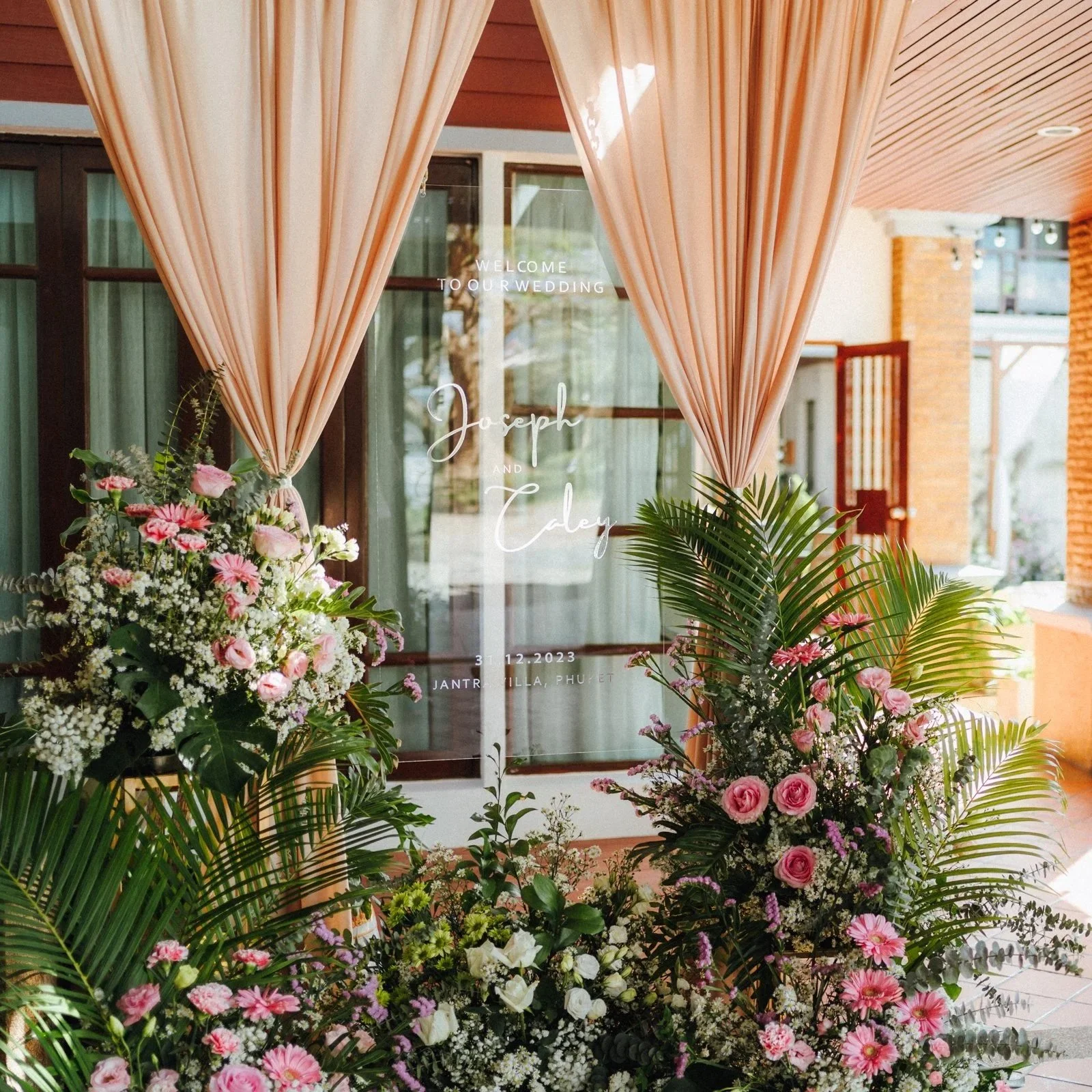 Decorative wedding sign with pink curtains and floral arrangements at a venue entrance.  Best wedding villa phuket.  Best wedding decoration Phuket