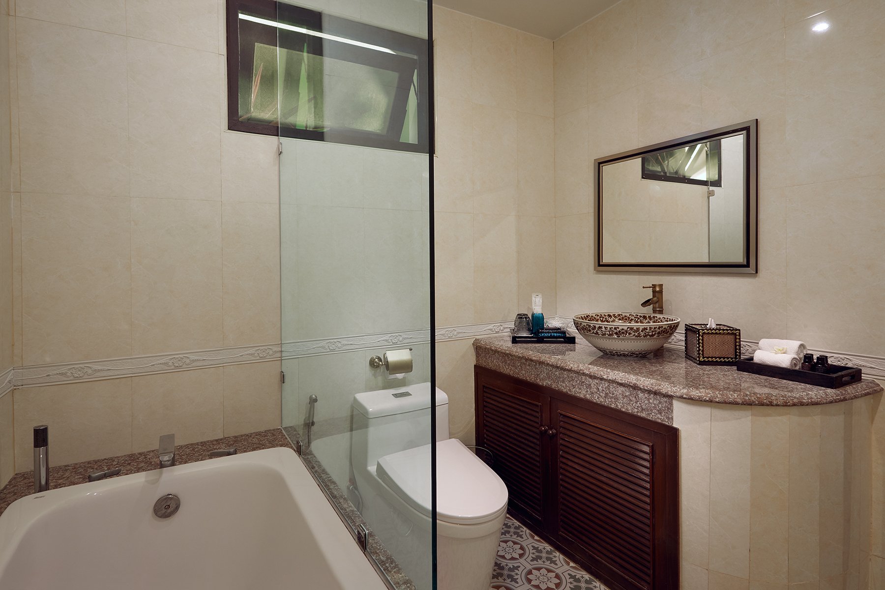 Modern bathroom featuring a large bathtub, a toilet, a marble countertop with a vessel sink, a mirror, and various toiletries and towels.
