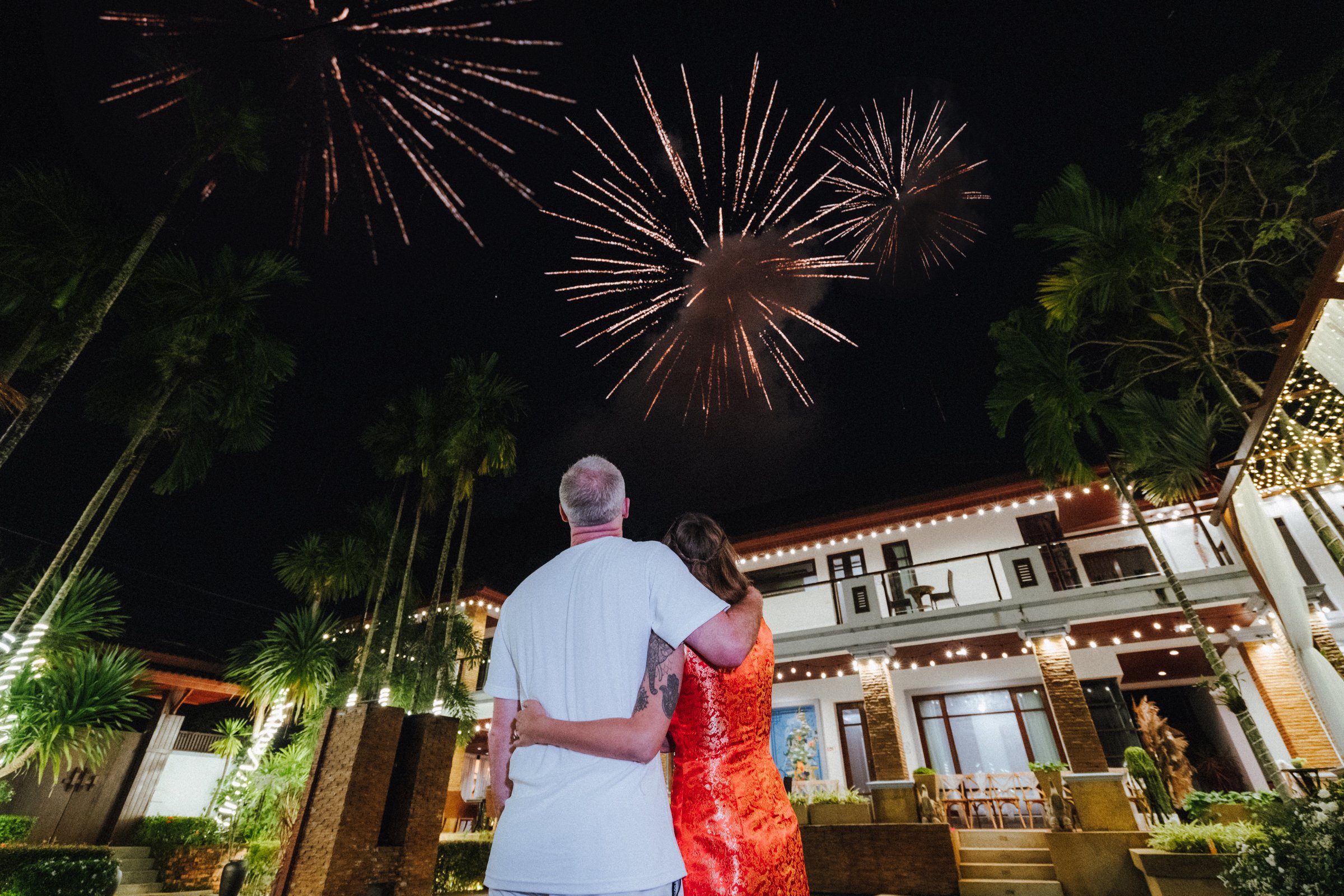 A man and woman stand together in a backyard, watching fireworks in the night sky.  Best villa for celebrations