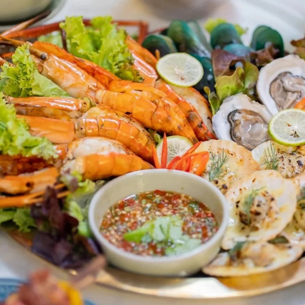 Seafood platter with prawns, oysters, and grilled fish, garnished with lemon slices and served with a dipping sauce with chili, lime, and herbs. Private villa dining