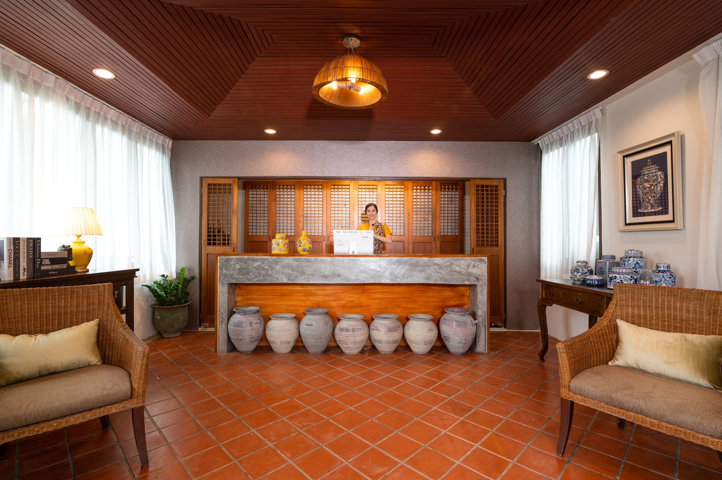 Villa reception area with wooden accents, ceramic vases beneath the counter, wicker chairs with pillows, a table with decorative objects on the right, a lamp, potted plant, and framed artwork.  Best villa for large groups