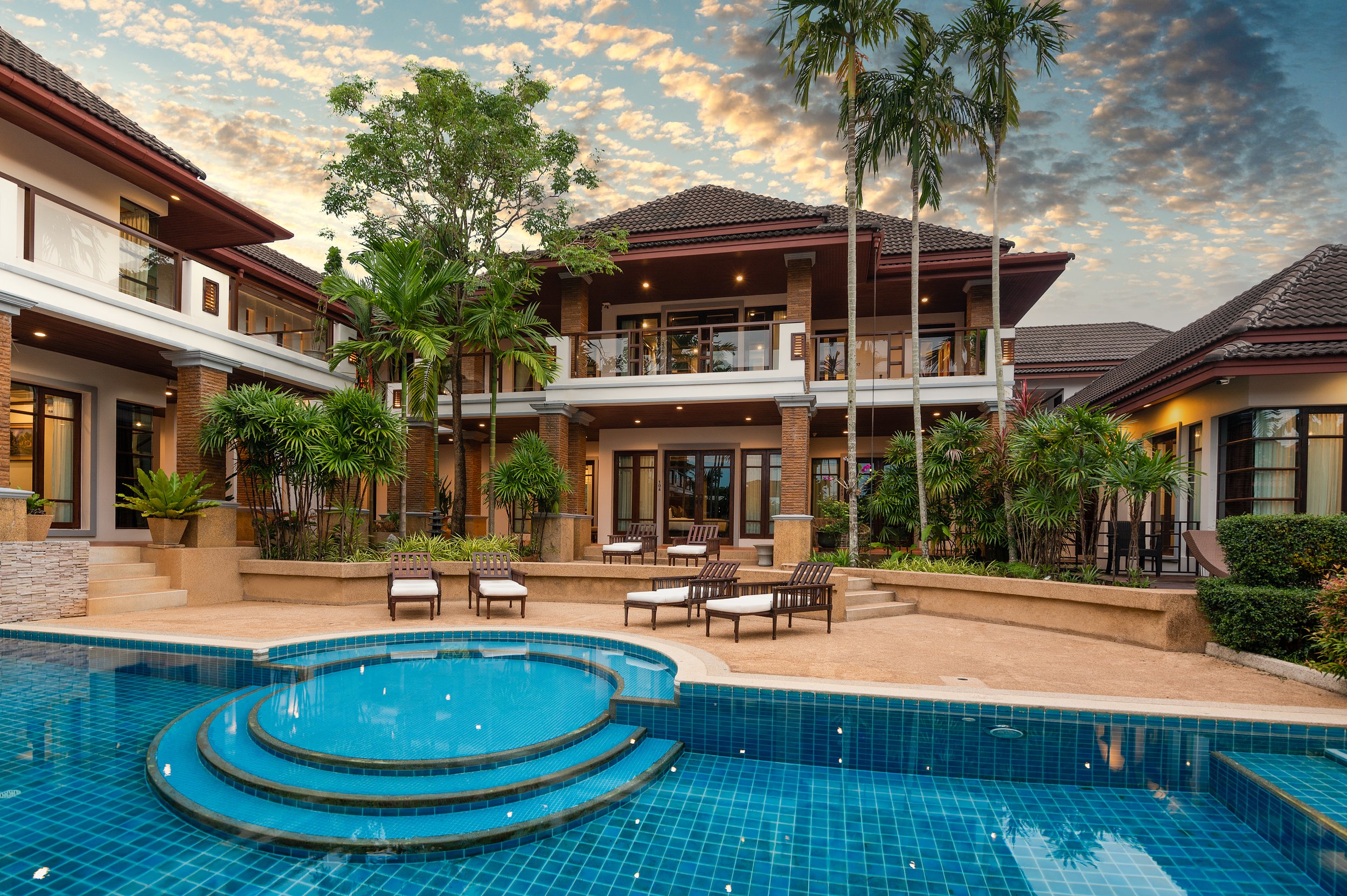 Luxury large group best villa Phuket with a swimming pool, outdoor seating, palm trees, and a sunset sky.
