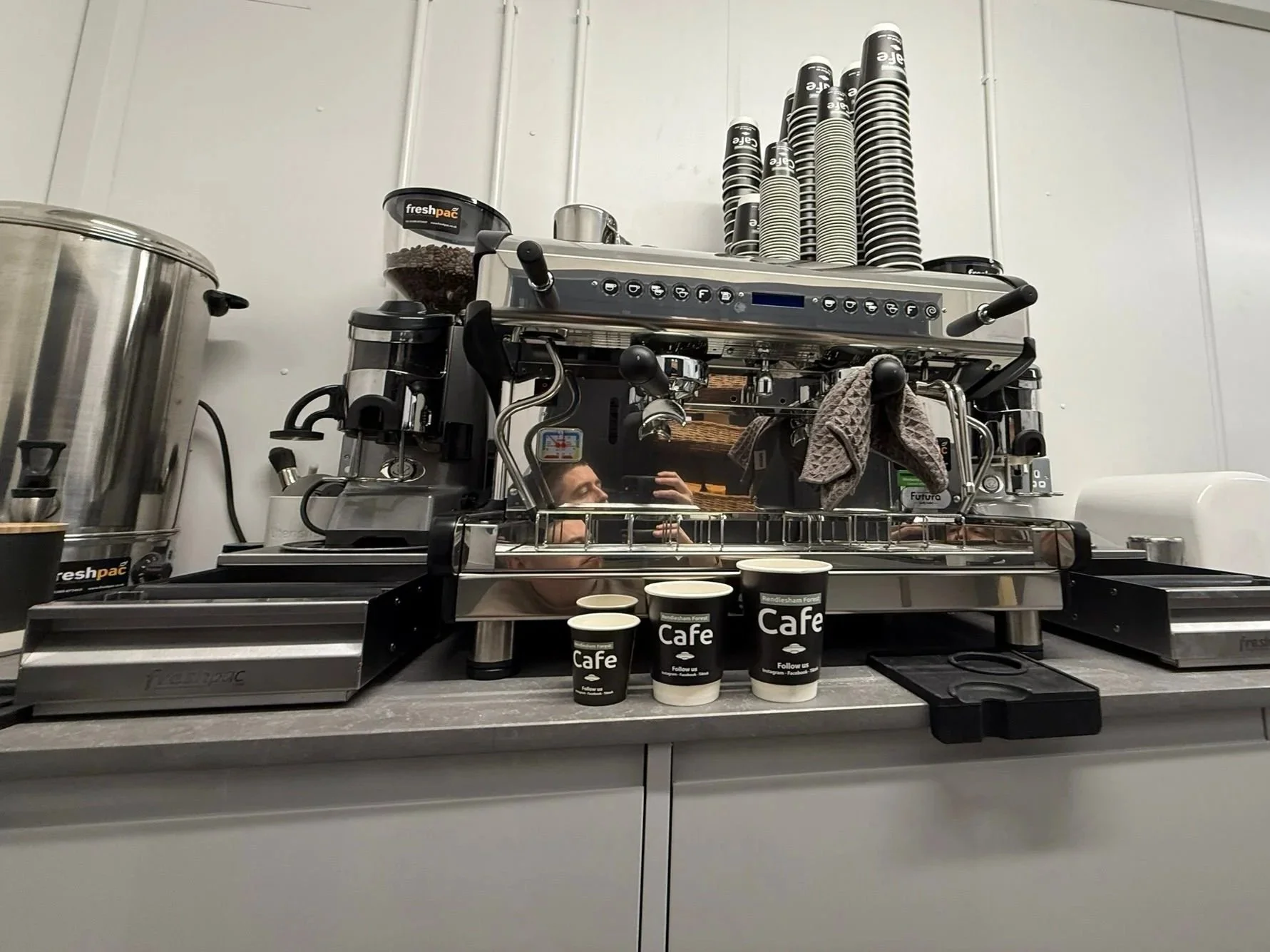 Coffee machine with cups, a grinder, and related equipment in a café setting.