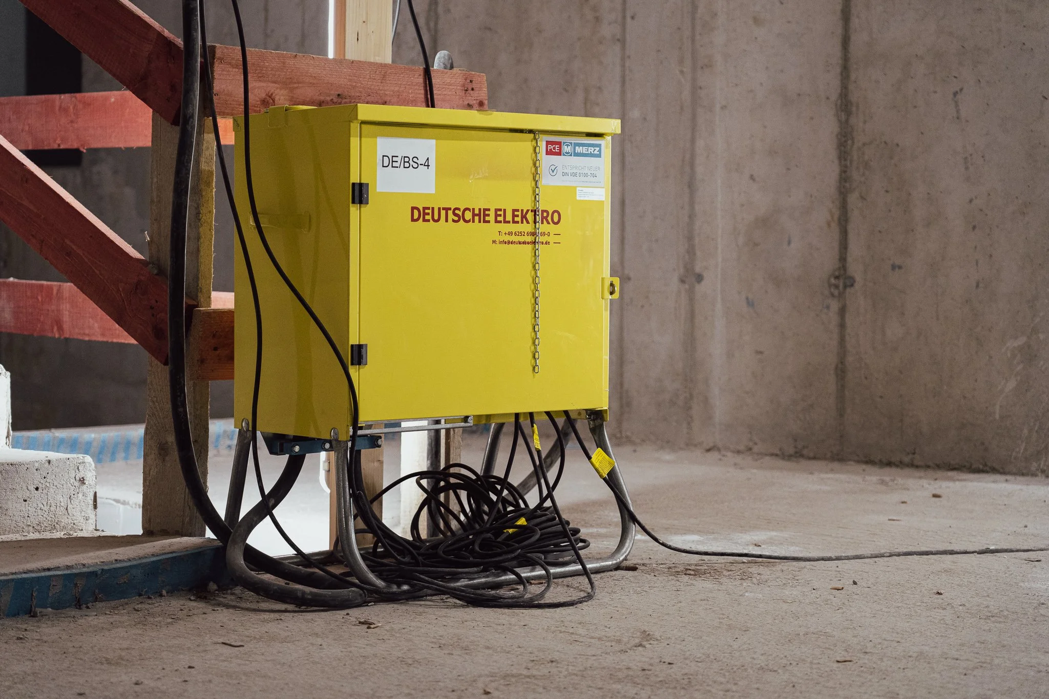 Gelbes Elektronik-Gehäuse an einer Baustelle, umgeben von schwarzen Kabeln.