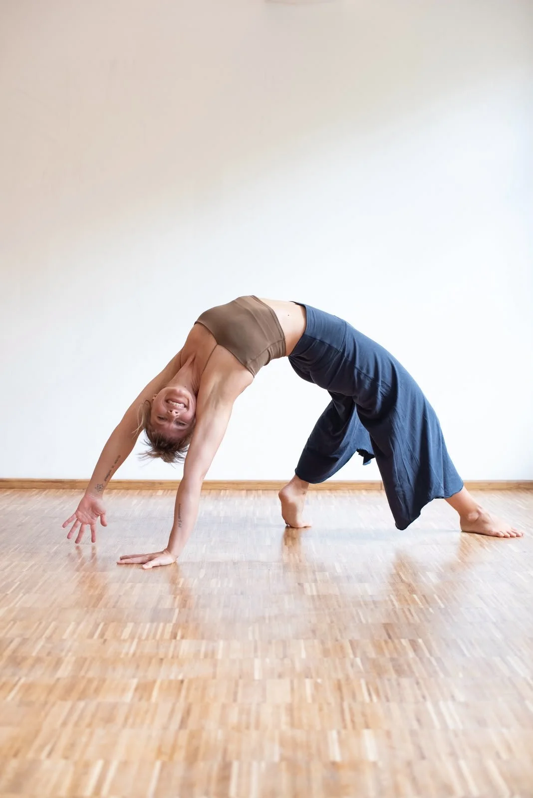 Junge Frau macht einen Handstand in einem Raum mit Holzfußboden und weißer Wand.