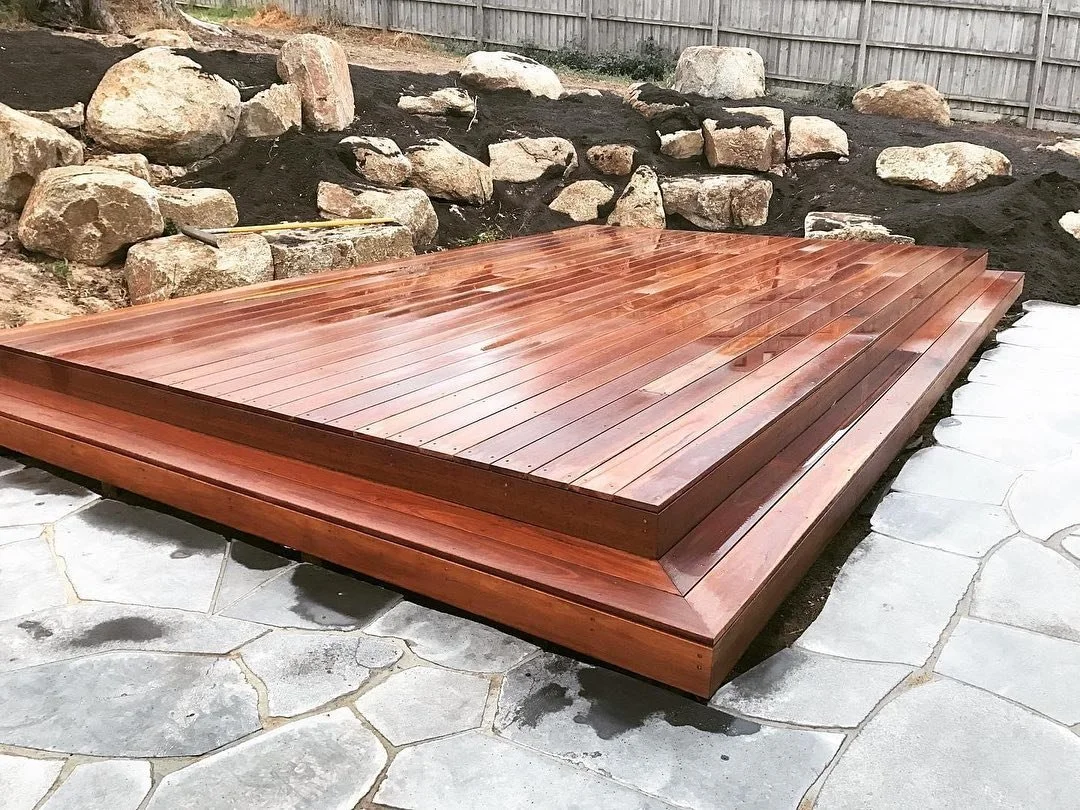 A newly built wooden hot tub or soaking tub on a stone patio, with a background of rocks and a wooden fence.