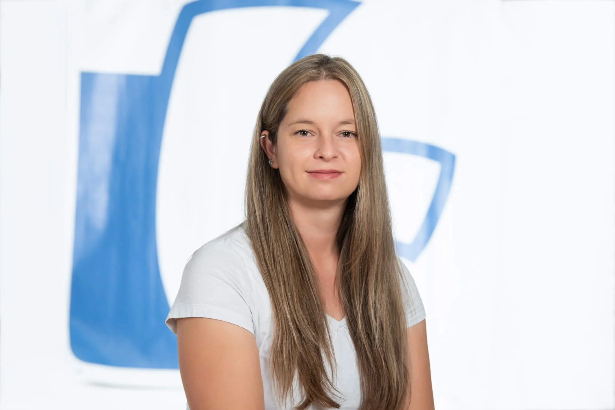 Frau mit langen braunen Haaren vor einem weißen Hintergrund mit blauer Logoschrift.