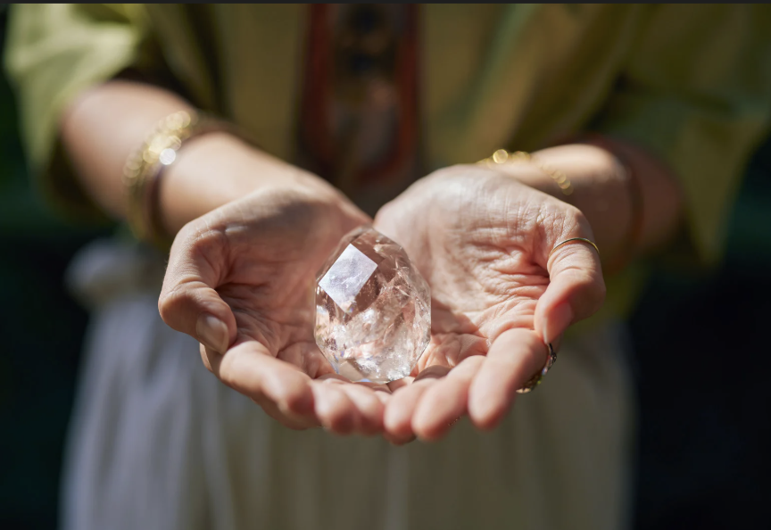 Person holding a large, clear quartz crystal in their hands.
