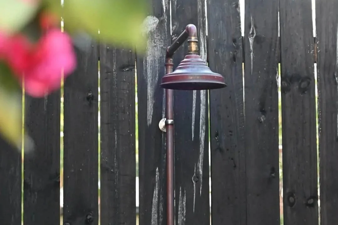 An outdoor garden shower head mounted on a dark wooden fence.