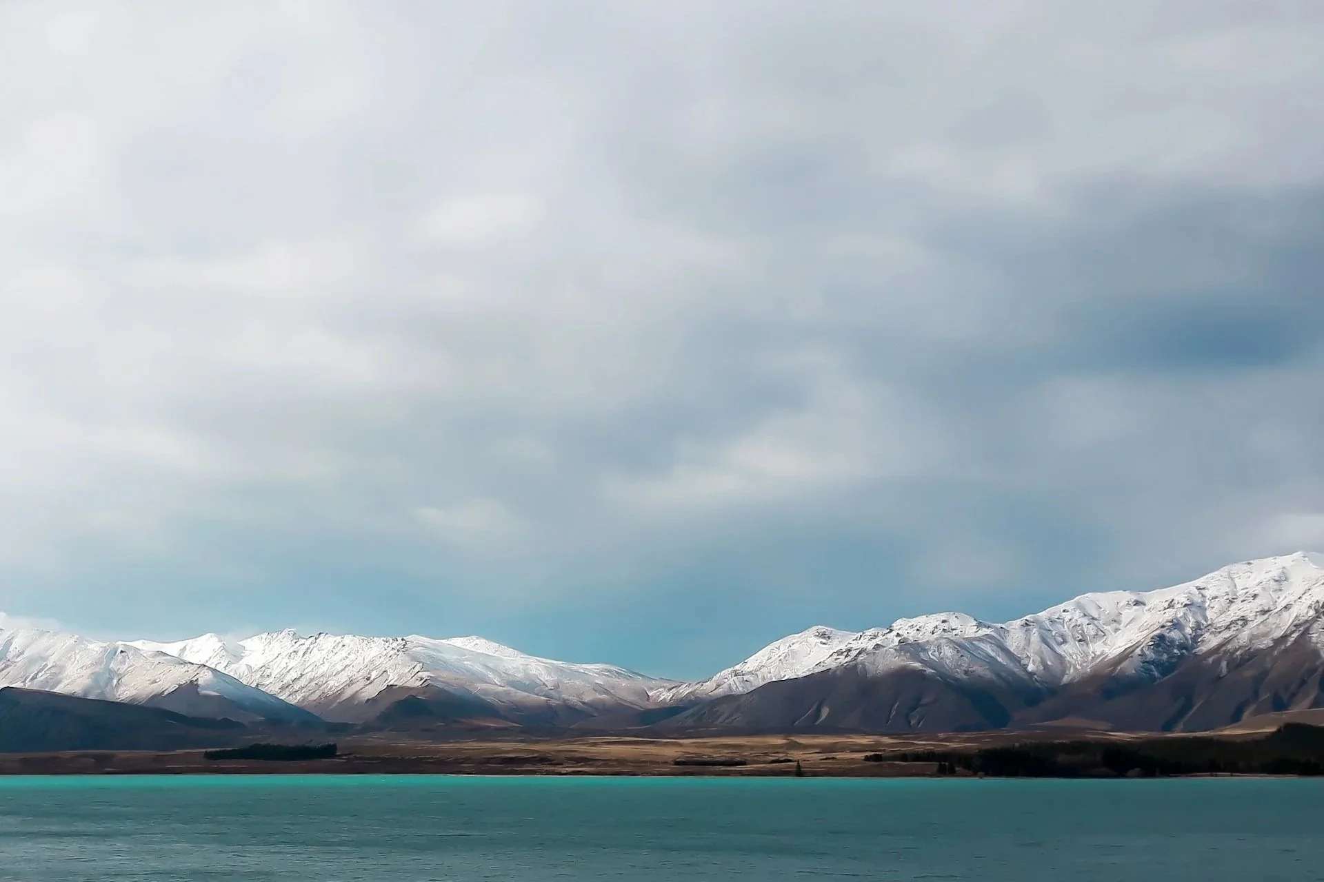 Snow-capped mountains over a body of water with a cloudy sky.