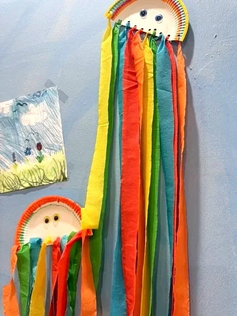 Bunte Papierfähnchen in Regenbogenfarben mit Smiley-Gesicht hängen an der Wand.