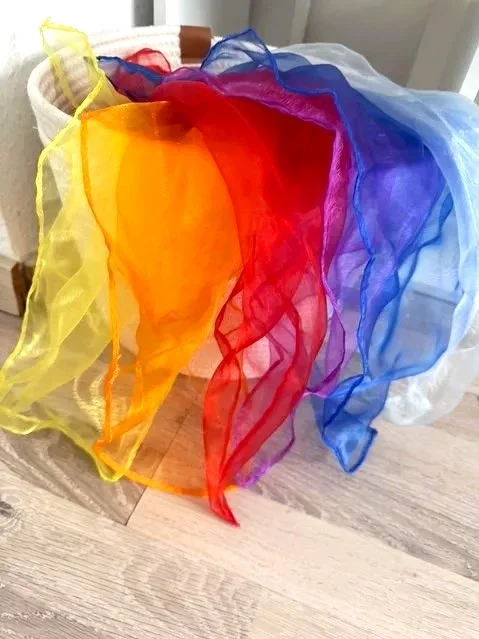 Bunte, transparente Tücher in den Farben Gelb, Orange, Rot, Pink, Blau und Weiß hängen an einem Korb.