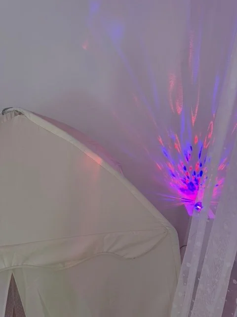 Bett mit weißem Bettbezug und bunte Lichtprojektion an der Wand
