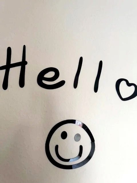 Wand mit dem Wort 'Hello' in schwarzer Schrift, ein Herz und ein lachendes Smiley-Gesicht unterhalb.