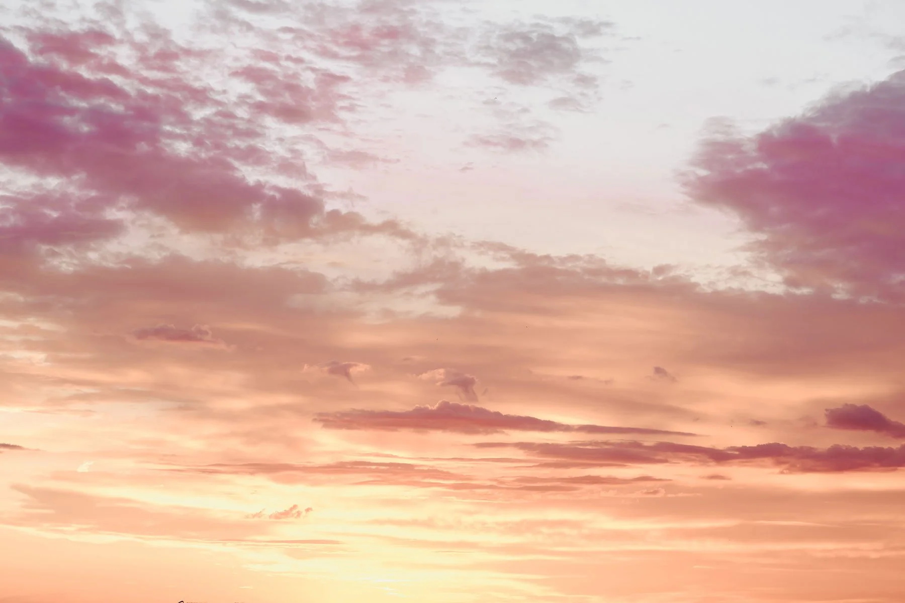 Der Himmel bei Sonnenuntergang mit Wolken in Pastellfarben, hauptsächlich rosa, lila und orange.