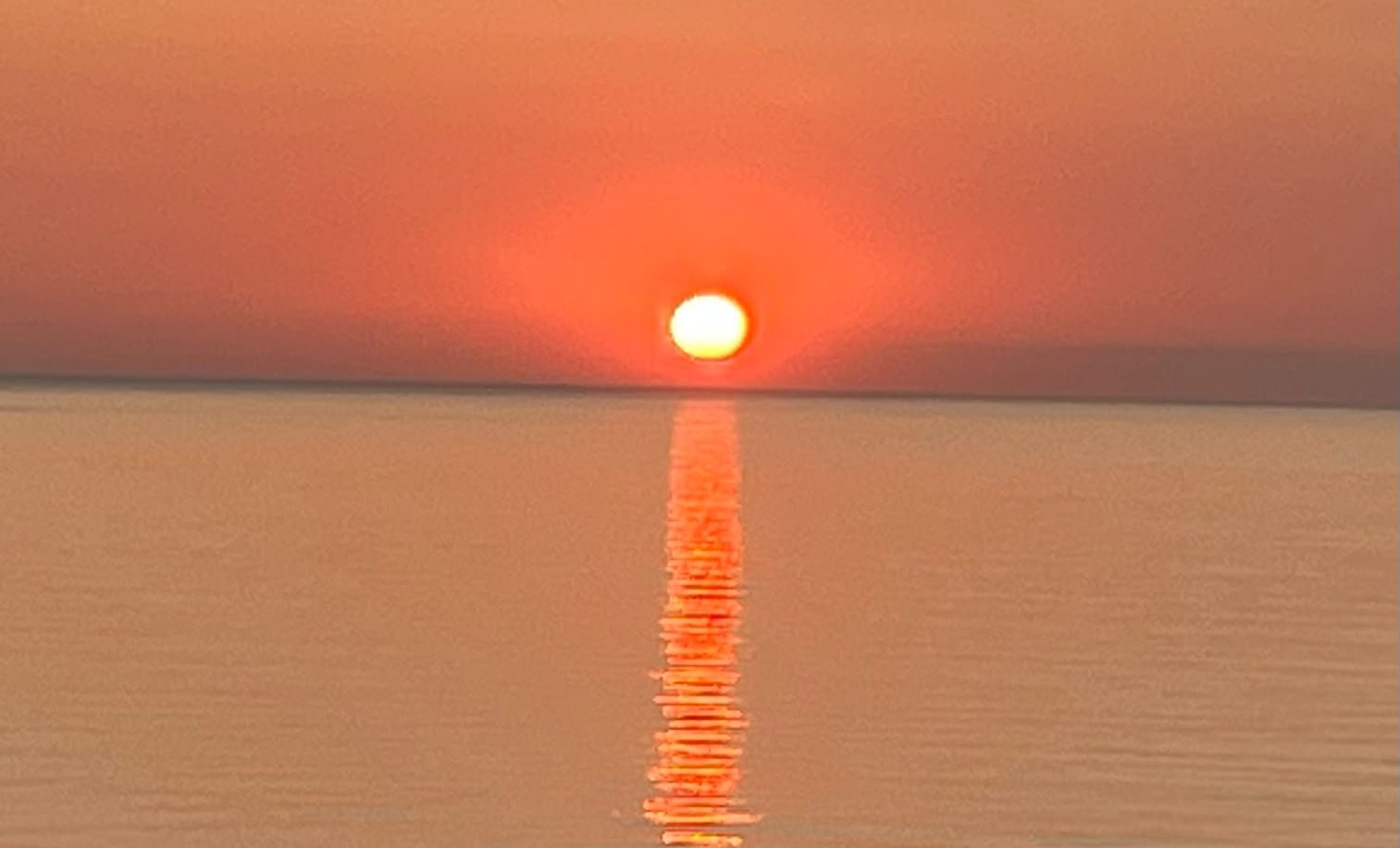 Sunset over calm water with a vibrant orange and pink sky, and the sun reflecting across the surface.