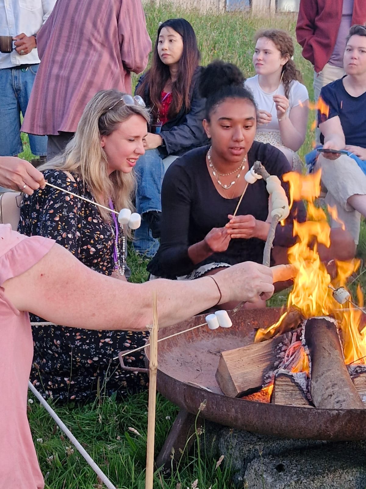 Group of people gathered around a campfire roasting marshmallows on sticks during an outdoor event.