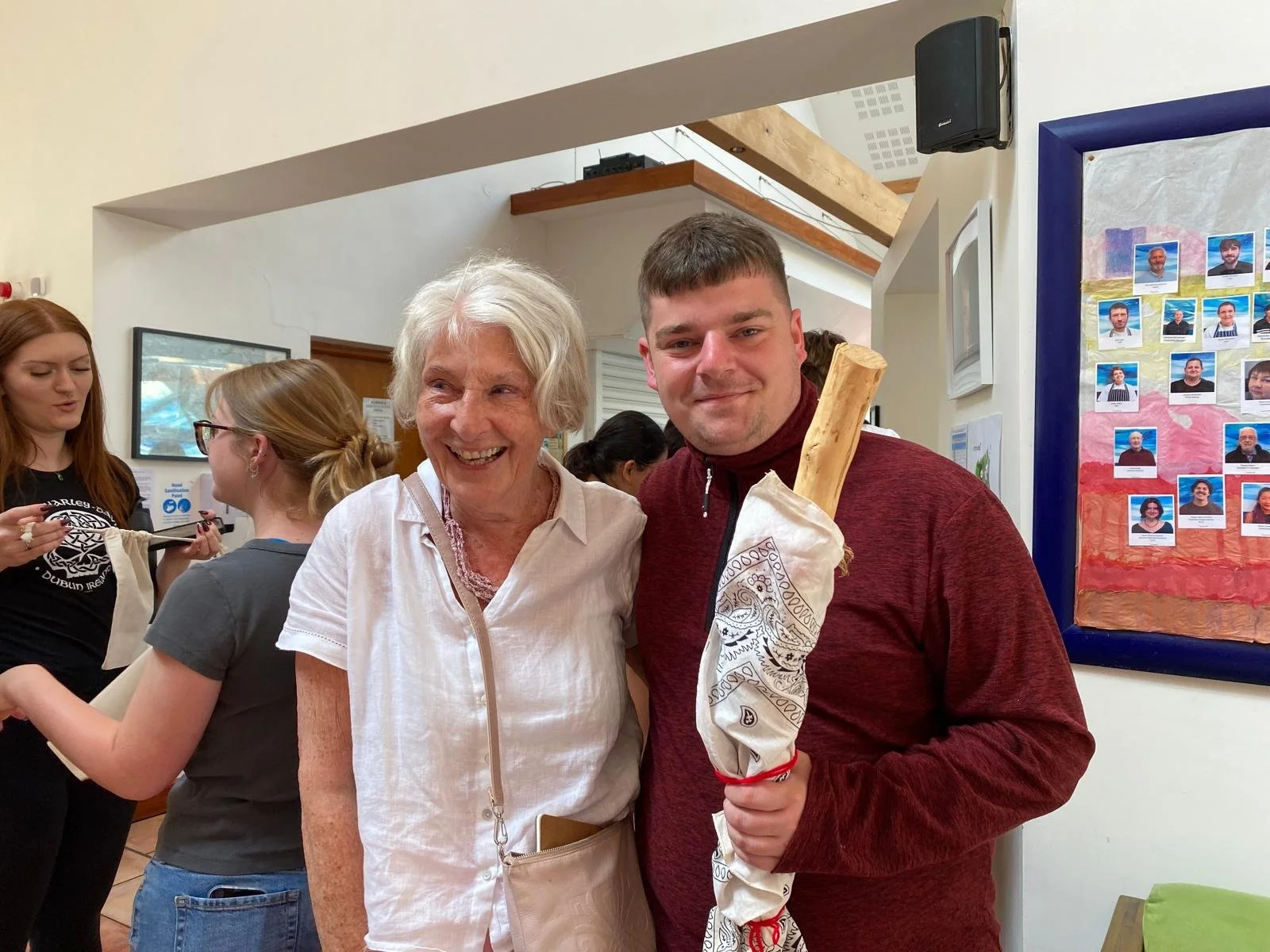 Dot Wilson and Aaron Smith smiling at the camera, holding a wooden talking stick wrapped in a bandana with a red band.