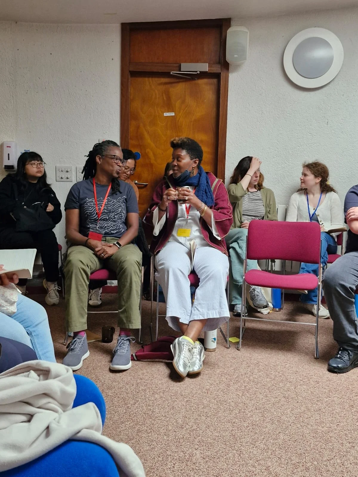 Group of women sitting and conversing in a room, with a wooden door and white walls.