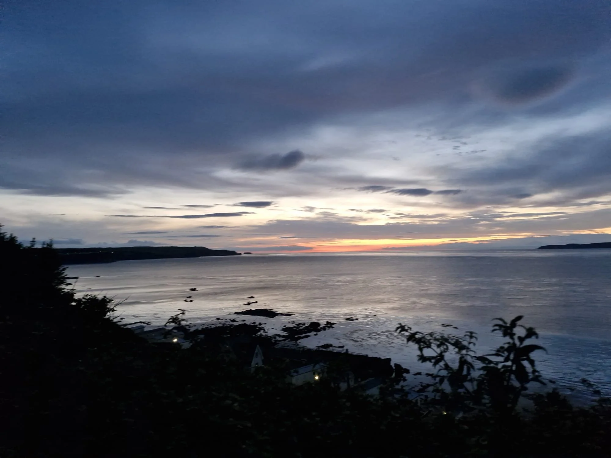View of a body of water during sunset with a cloudy sky and distant landforms.