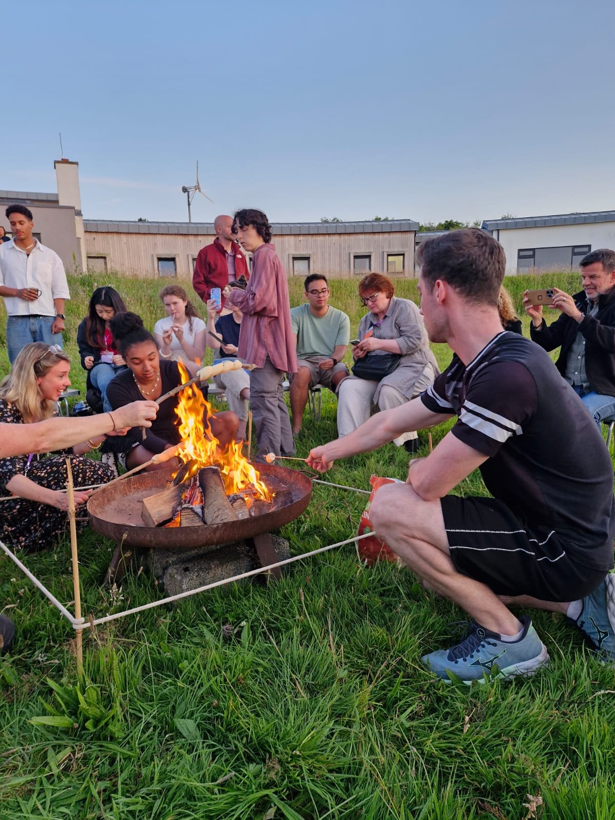 People gathered around a campfire roasting marshmallows outdoors during evening.