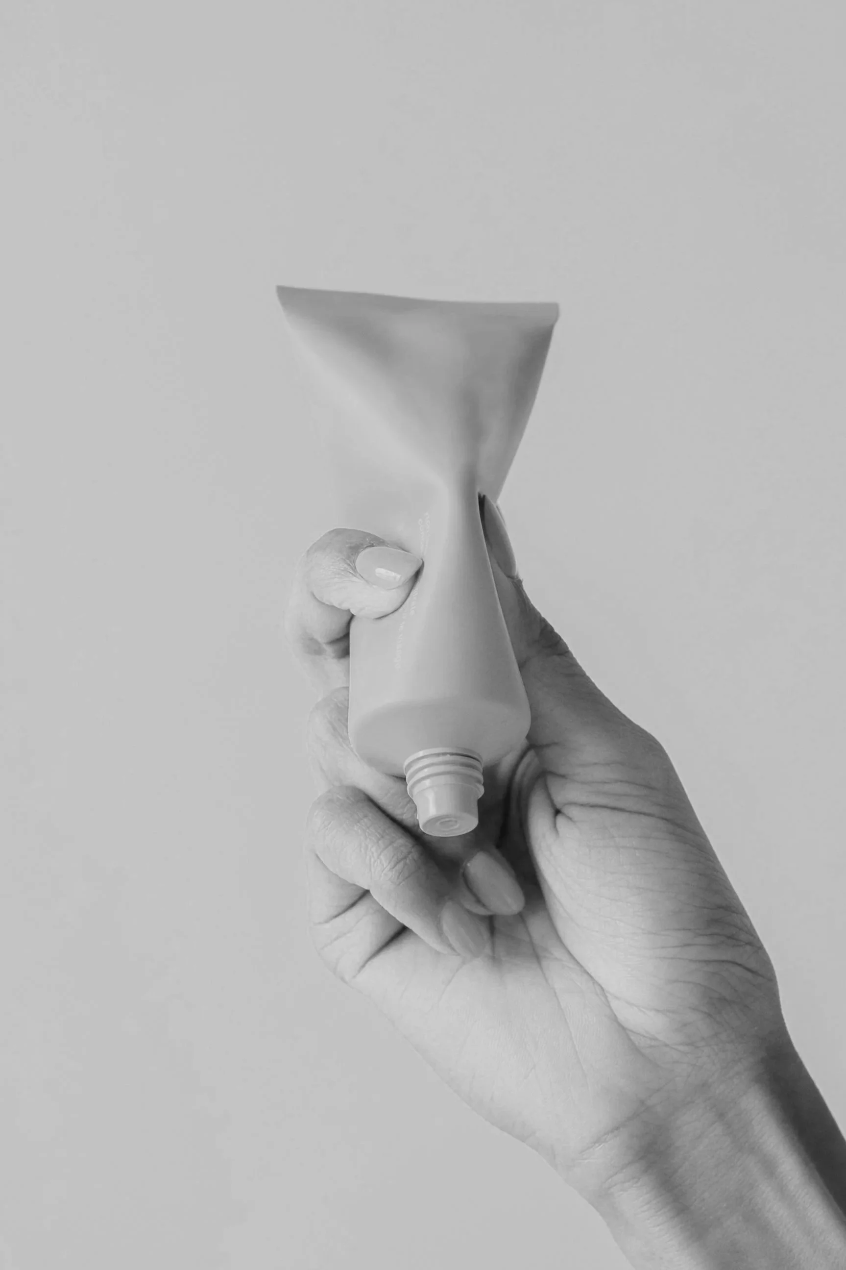 A hand holding a partially squeezed tube of cream or lotion against a plain background.
