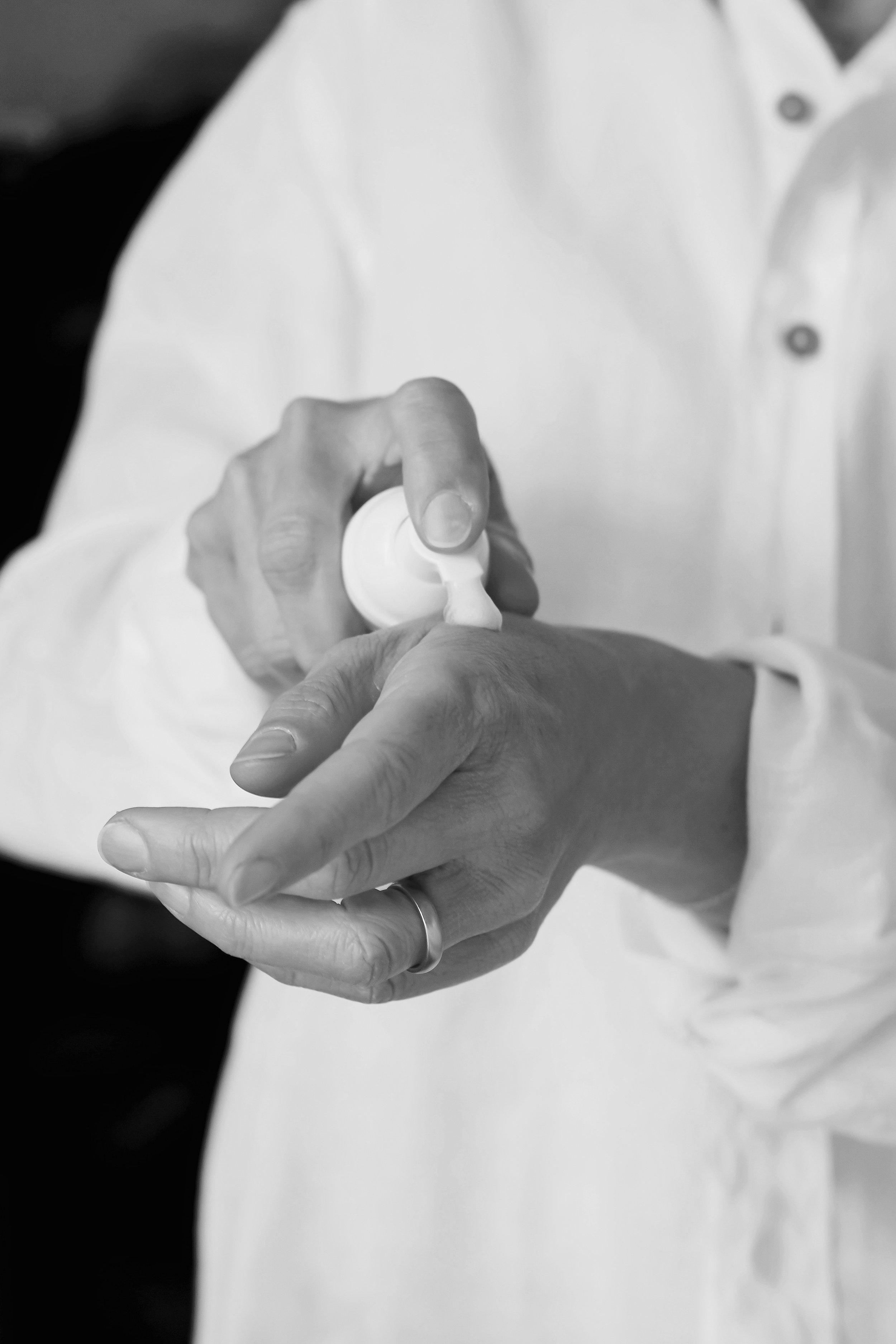 A person applying lotion or cream to their hand in a black-and-white photo.