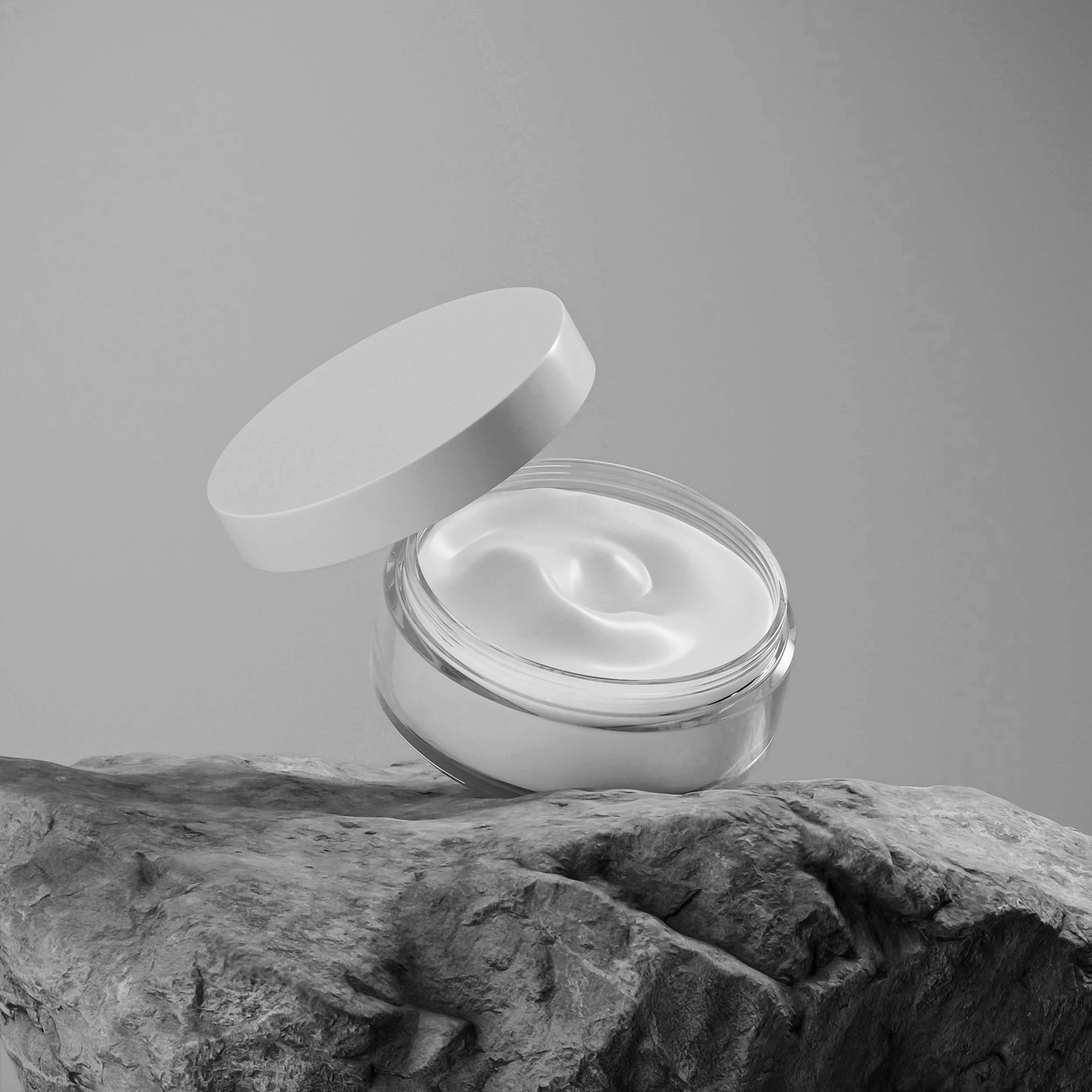 A jar of cream with the lid partially off, placed on a textured rock surface against a plain background.