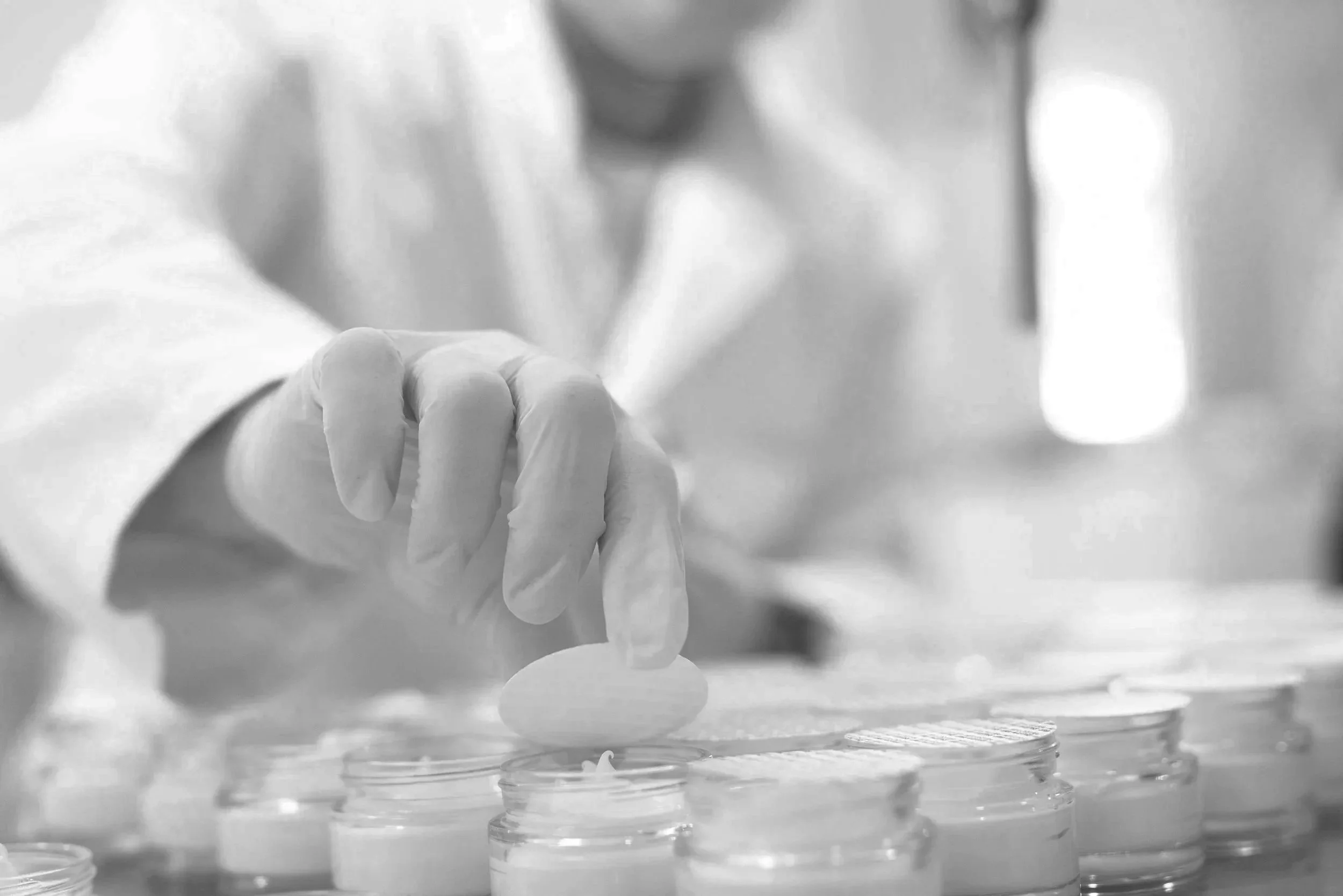 Close-up of a scientist wearing gloves and a lab coat, handling a test tube or vial, with lab containers in the foreground in a laboratory setting