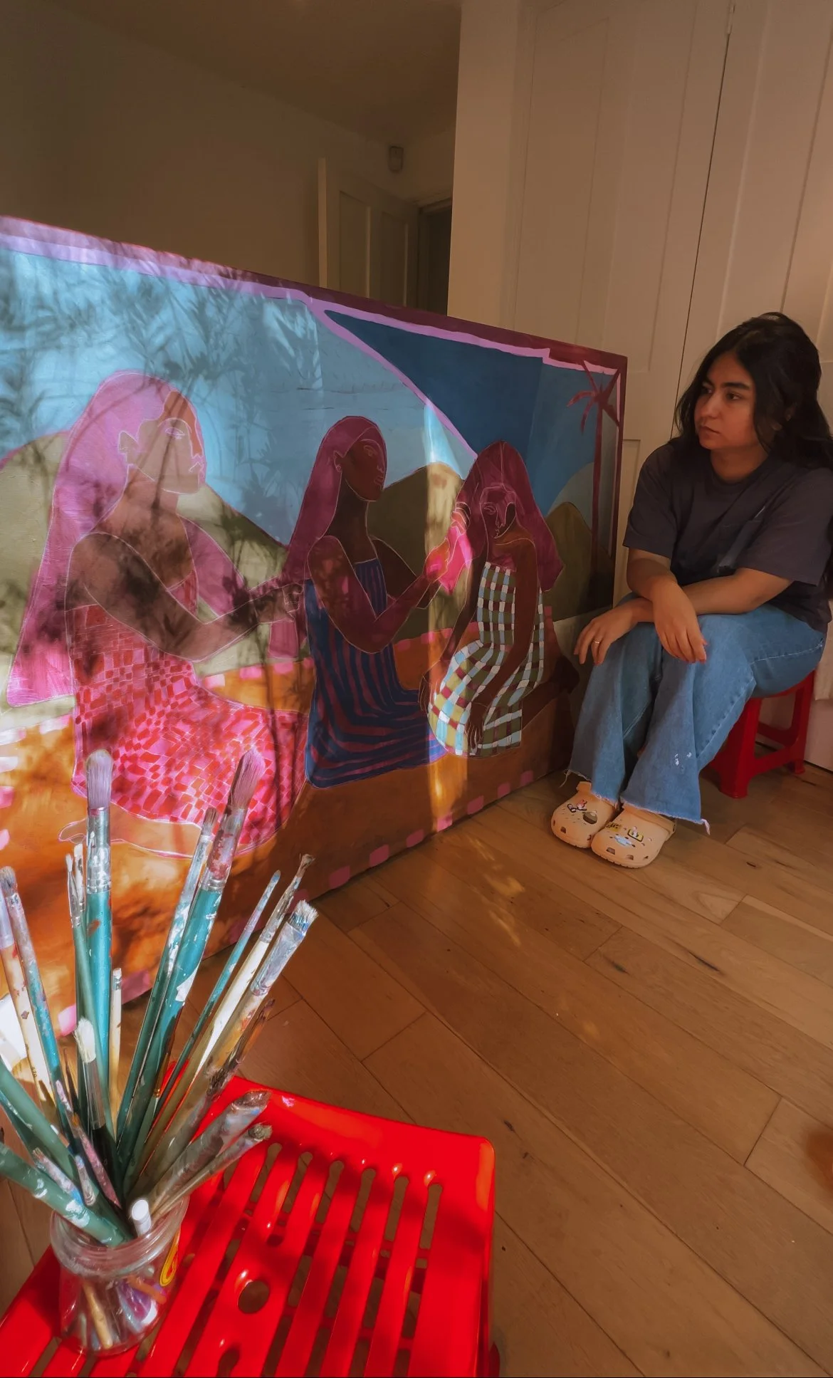 Self taught artist, Zuleika Evans observing her art piece of three women painted on a canvas, inspired by time spent travelling in the Philippines.