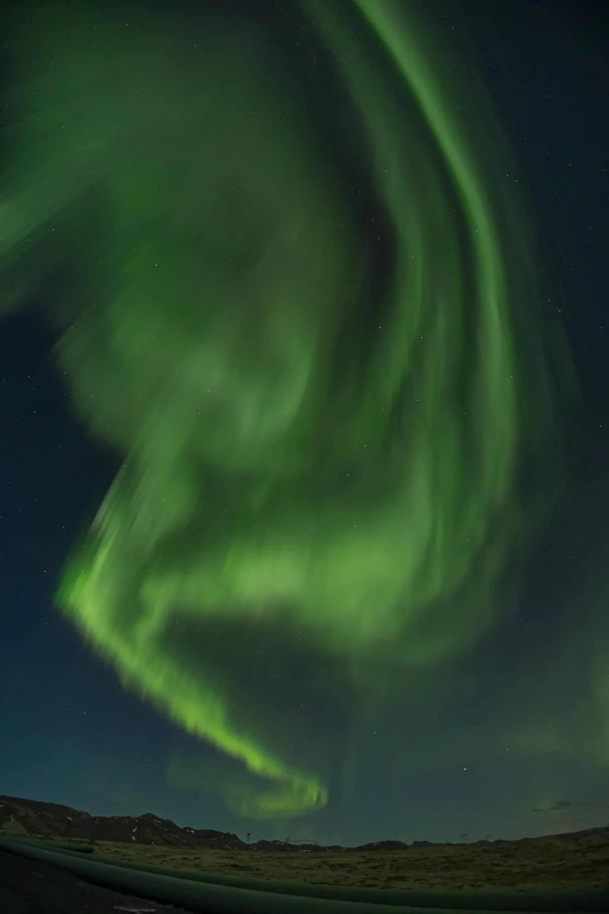 Northern lights (aurora borealis) glowing green in the night sky over a landscape.