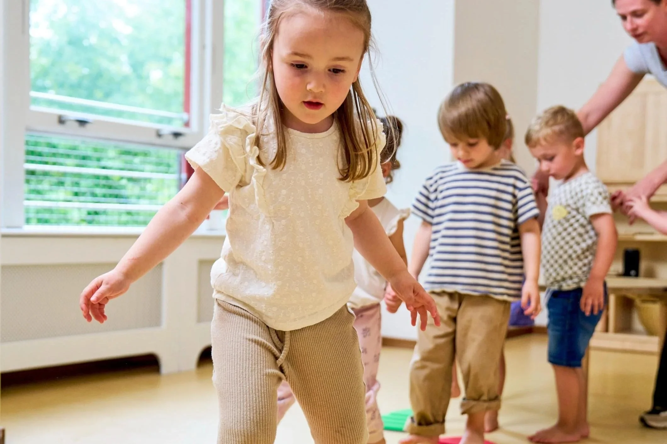 Kinderen die op blote voeten in een kring bewegen in een kamer met grote ramen.