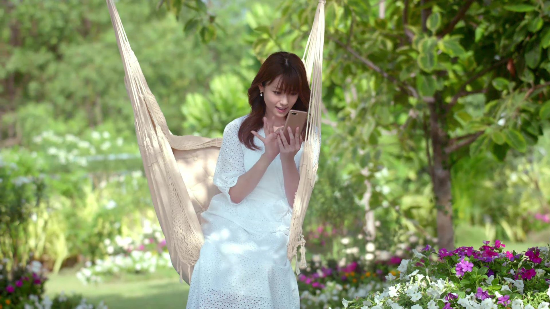 庭のハンモックに座る若い女性がスマートフォンを見ている風景