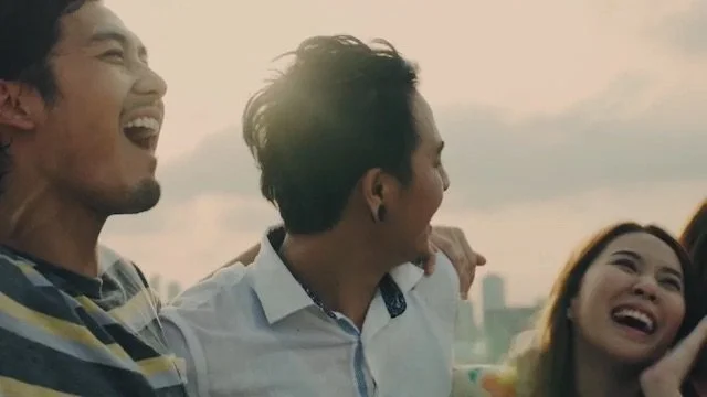 3人の若い男女が笑顔で楽しそうにしている。背景は空とビルが見える都市風景。