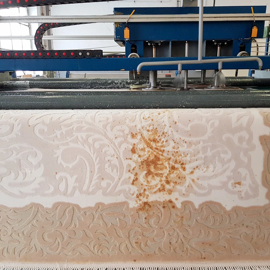 Ein industrieller Druckprozess auf einer Wand mit ornamentalem Muster, bei dem eine braune Flüssigkeit oder Farbe aufgetragen wird.