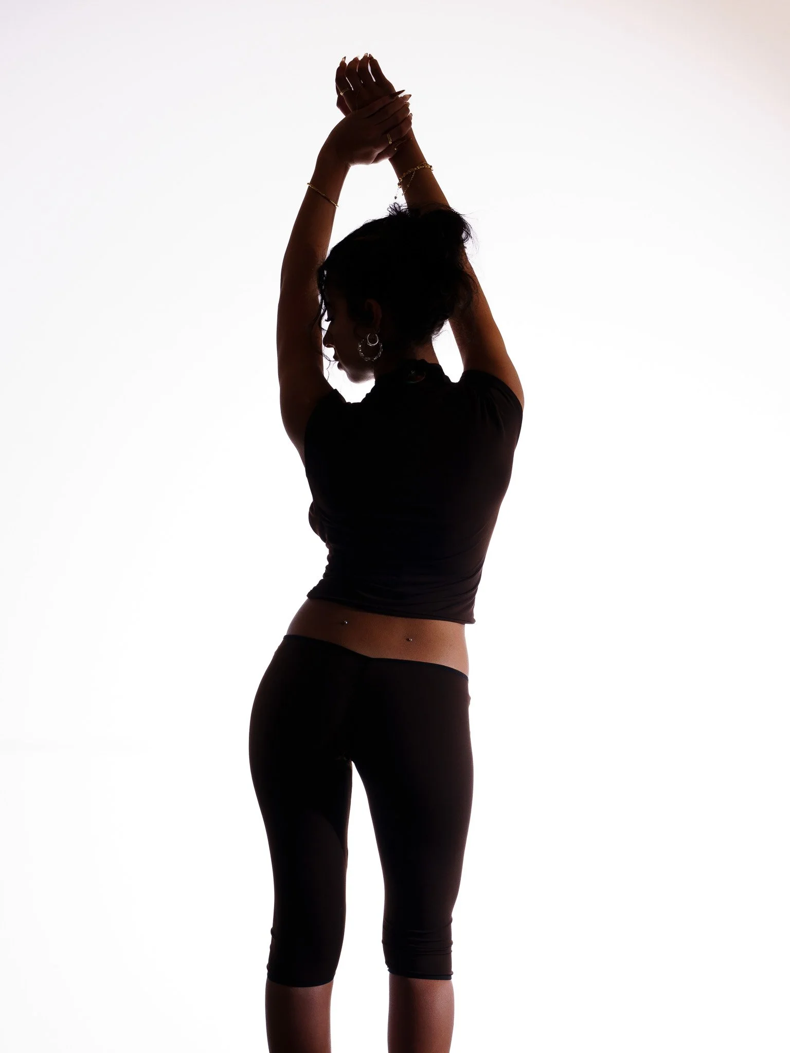 Silhouette of a woman with her hands raised above her head, wearing a black athletic outfit and standing against a white background.