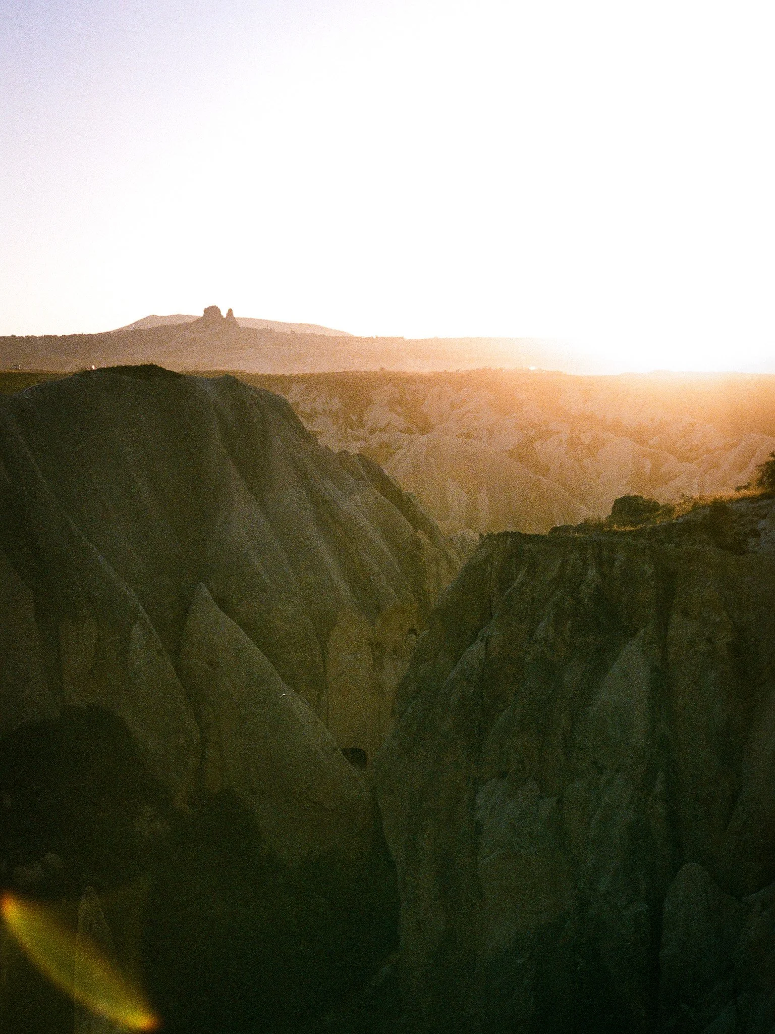 Sunset over a rugged canyon with large rock formations and hills in the background.