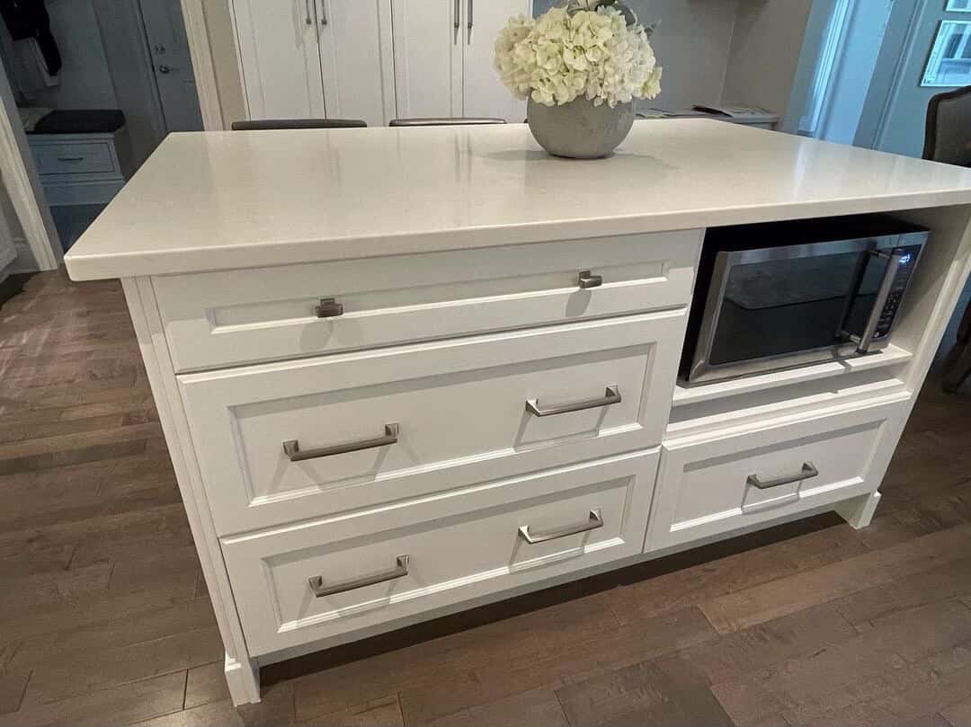 A white kitchen island with four drawers and a built-in microwave oven, with a flower vase on top, in a home kitchen. Cabinet refinishing in franklin TN