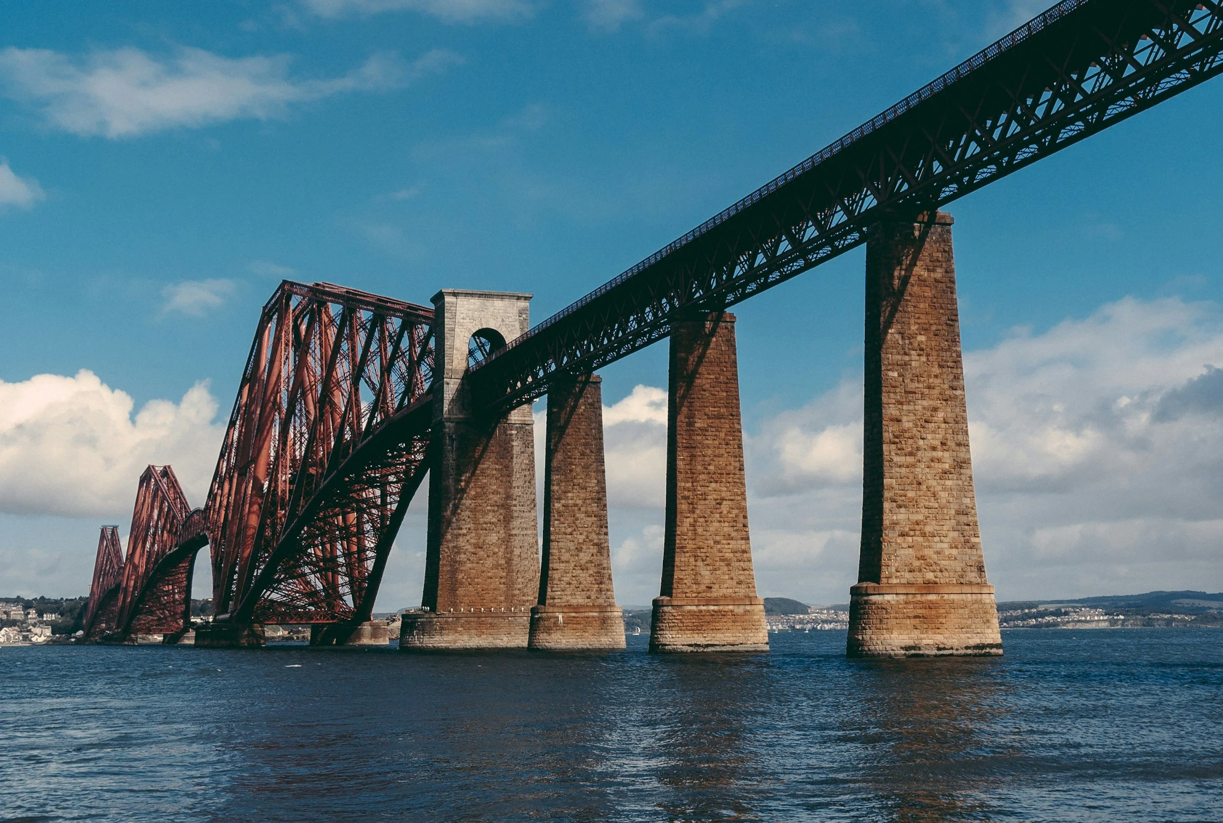 A large bridge spanning over a body of water with a mix of metal and stone supports beneath a partly cloudy sky.