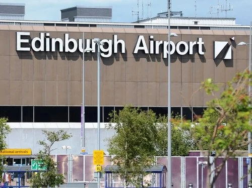 Sign at Edinburgh Airport with trees and parking lot in foreground.
