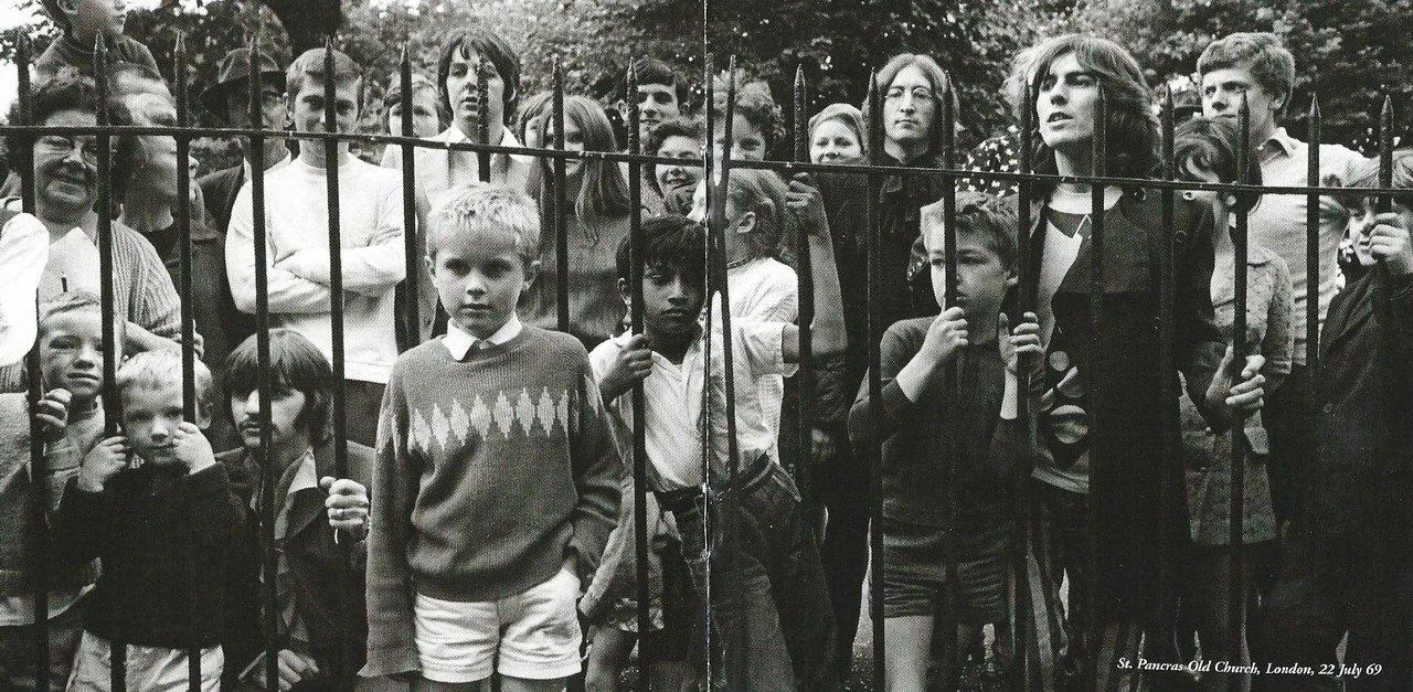 The Beatles and a group of children standing behind a wrought-iron fence, some looking directly at the camera, at St. Pancras Old Church in London, July 22, 1969.