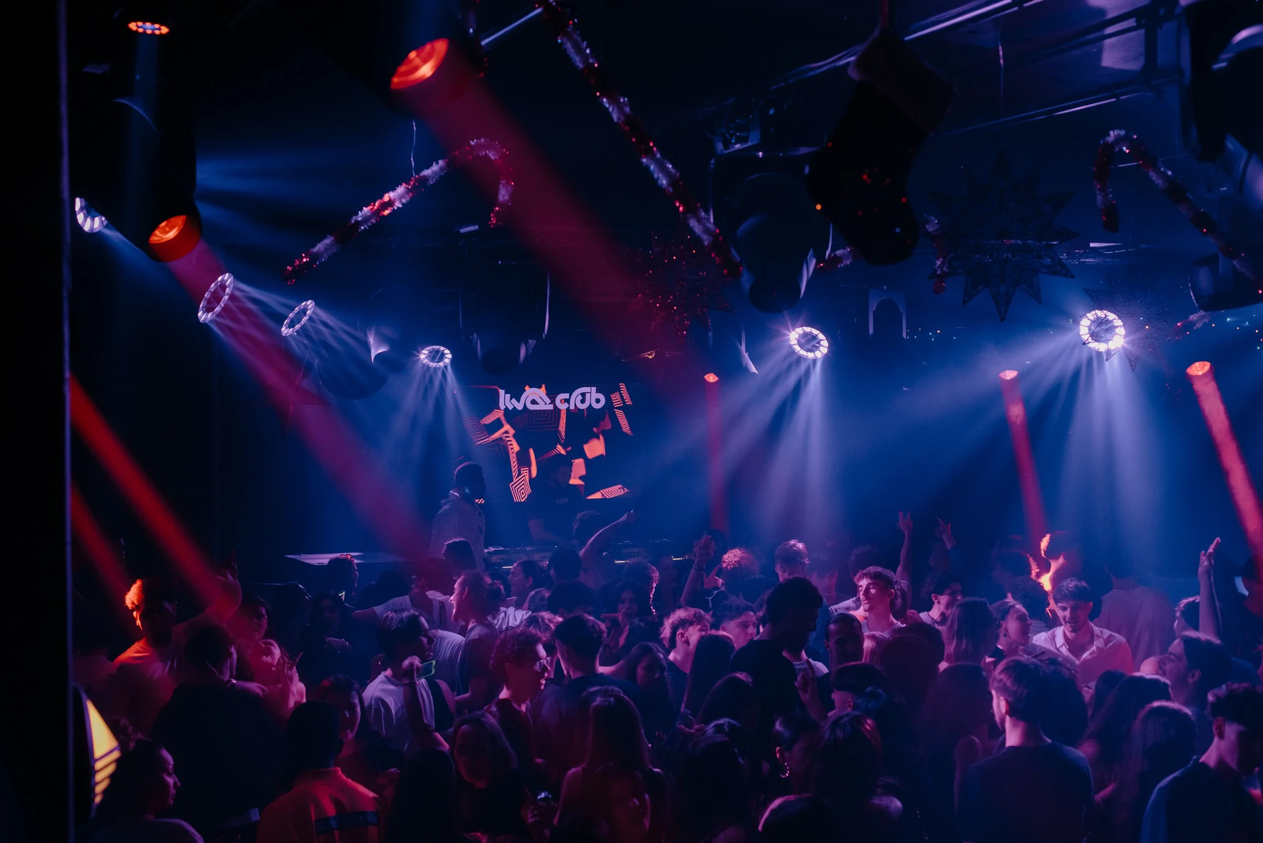 Une scène de concert ou de fête avec des lumières colorées, un public nombreux et un DJ sur scène.