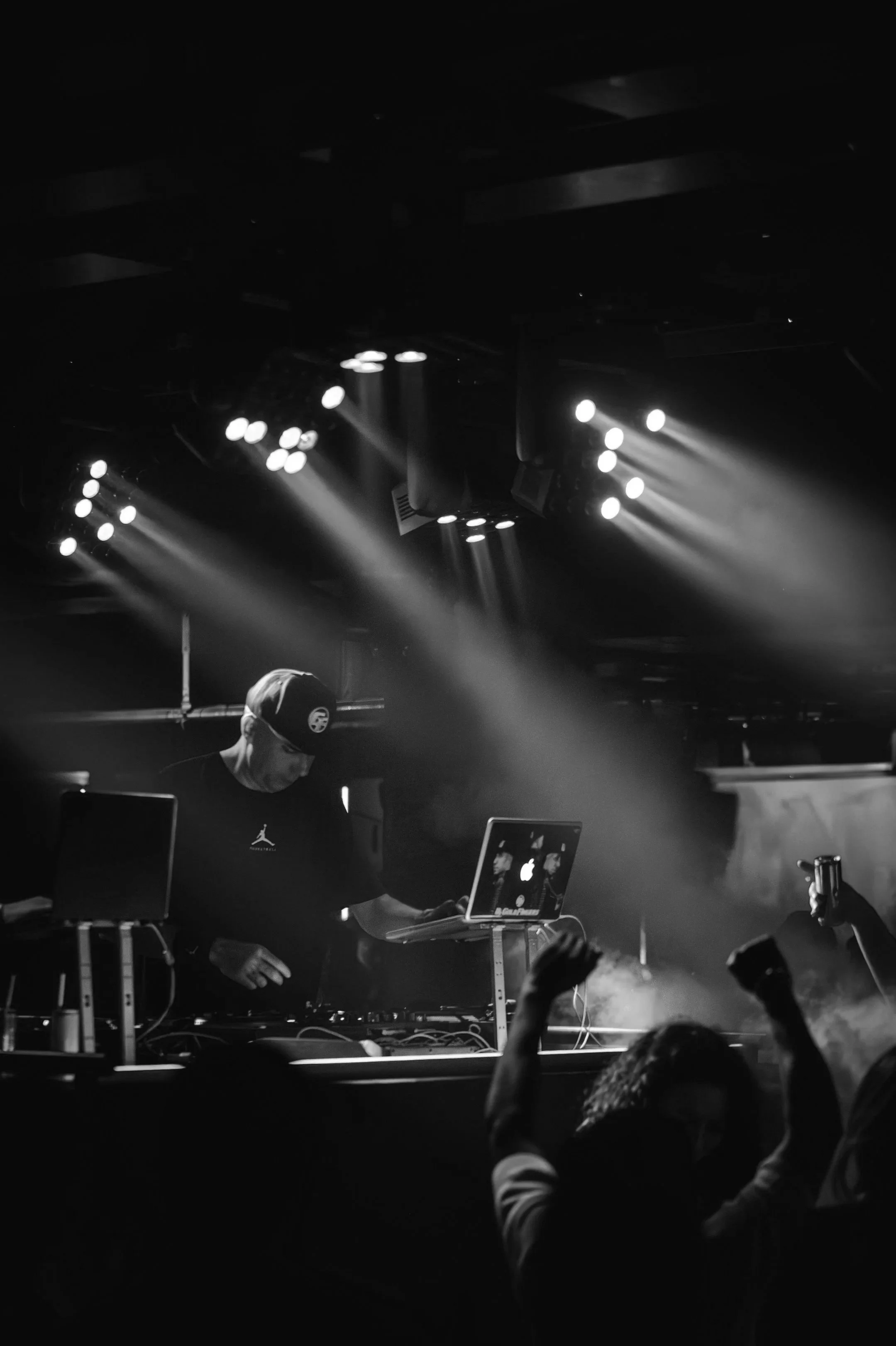 DJ performatif dans une boîte de nuit, éclairage lumineux sur scène, public avec bras levés, ambiance sombre et dynamique.