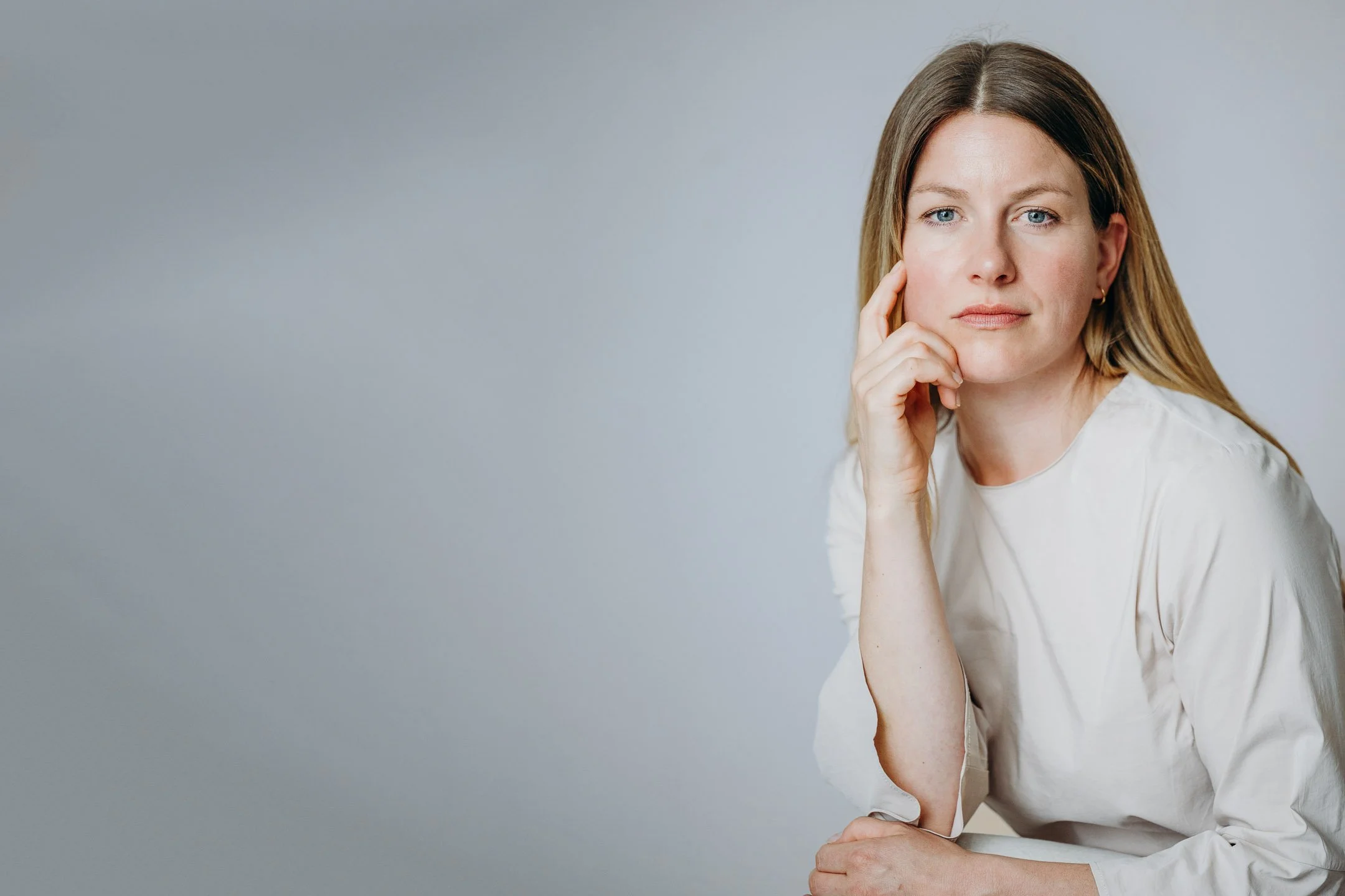 Professionelles Business Portrait einer Frau vor neutralem Hintergrund in einer reflektierten Pose mit aufgestütztem Kinn.