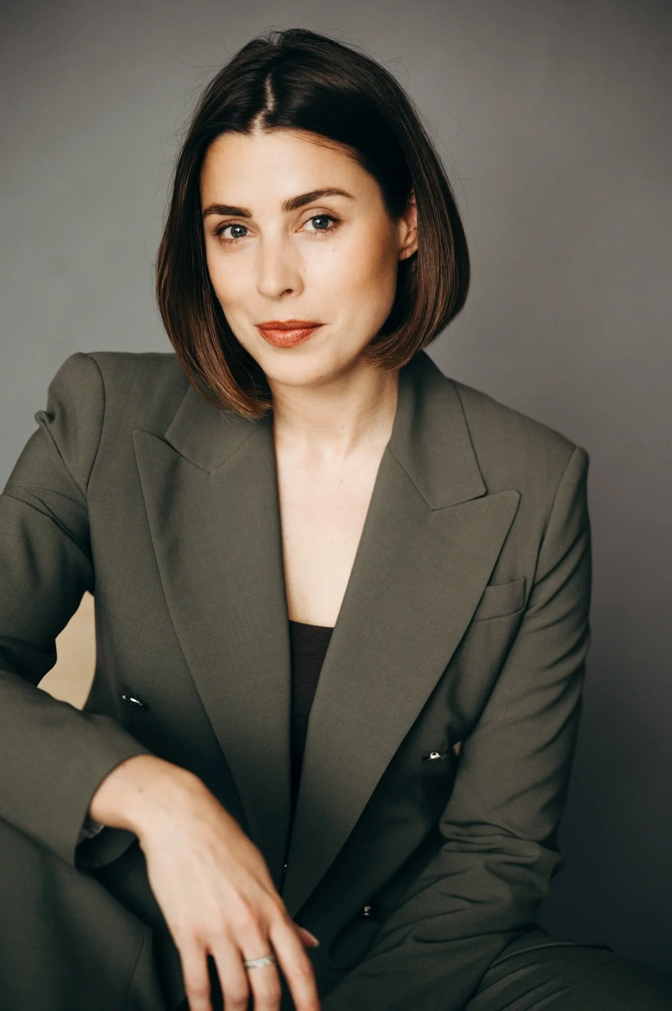 Business Porträt einer jungen Frau im olivgrünen Anzug sitzend auf einem Stuhl