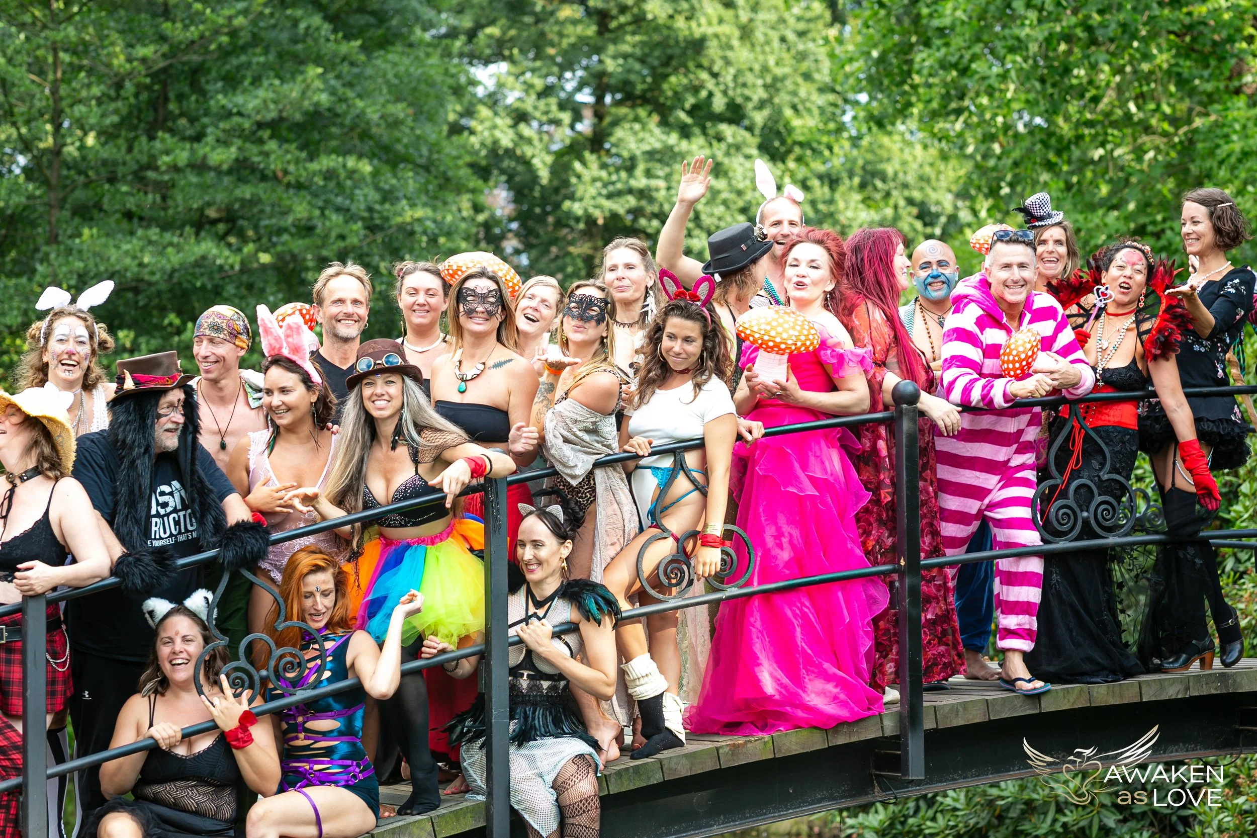 Group of people at a Tantra Festival dressed in colorful, whimsical costumes standing on a bridge outdoors, smiling and celebrating.